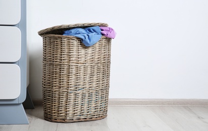 Photo of Laundry basket with dirty clothes on floor at wall, space for text