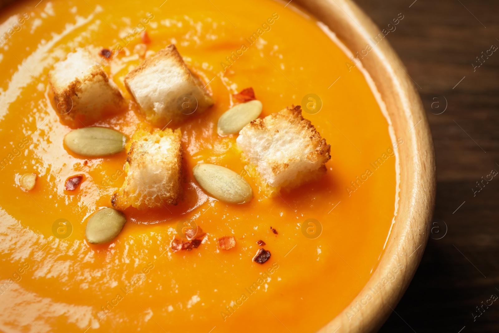 Photo of Bowl with tasty pumpkin cream soup on wooden table, closeup