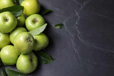 Photo of Ripe green apples with leaves on dark grey table, flat lay. Space for text