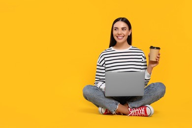 Happy woman with laptop holding paper cup on orange background, space for text