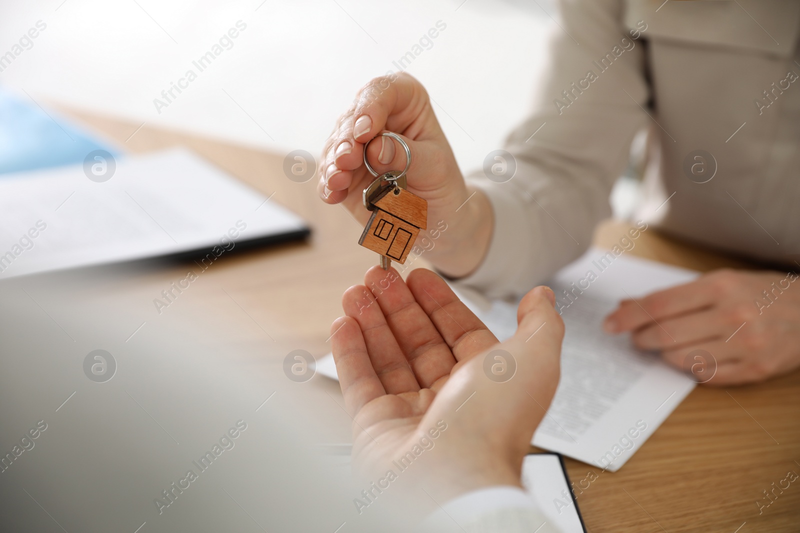 Photo of Real estate agent giving key with trinket to client in office, closeup