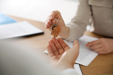 Real estate agent giving key with trinket to client in office, closeup