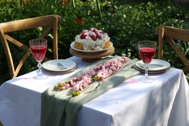 Beautiful spring flowers, delicious cake and wine glasses on table in garden