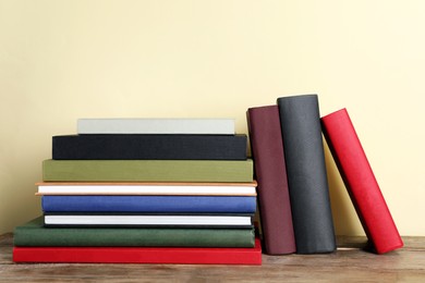 Photo of Many hardcover books on wooden table near yellow wall