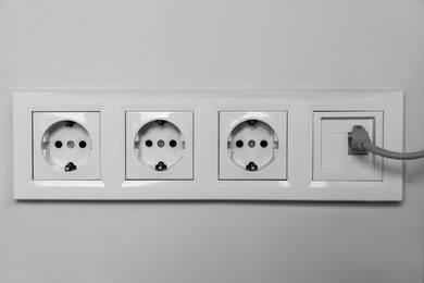 Photo of Power sockets with internet cable on white wall, closeup. Electrical supply