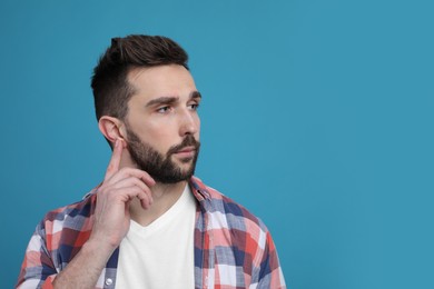 Photo of Man pointing at his ear on light blue background. Space for text