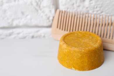 Photo of Orange solid shampoo bar and comb on white table, closeup. Space for text