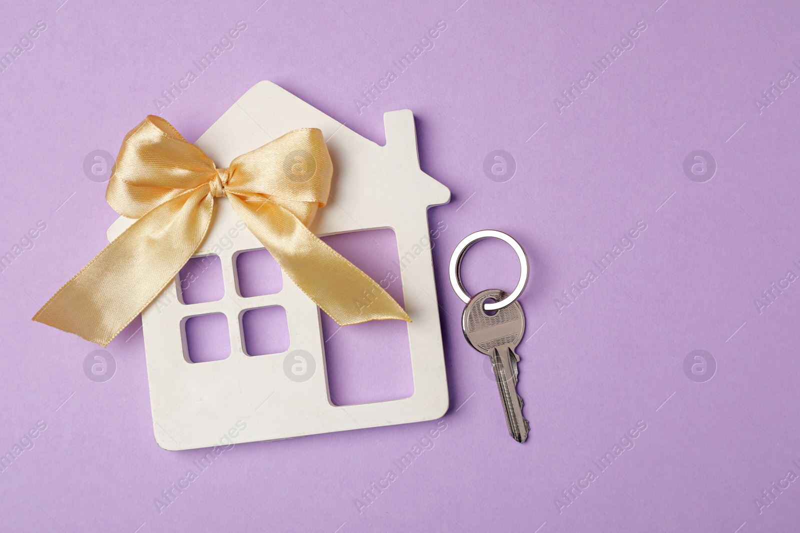 Photo of House model with bow and key on violet background, flat lay. Housewarming party