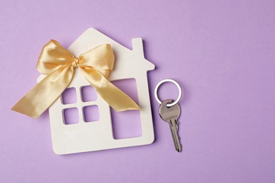 Photo of House model with bow and key on violet background, flat lay. Housewarming party