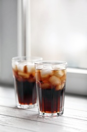 Photo of Glasses of cola with ice near window, space for text