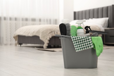 Different cleaning supplies in bucket on floor at home, space for text