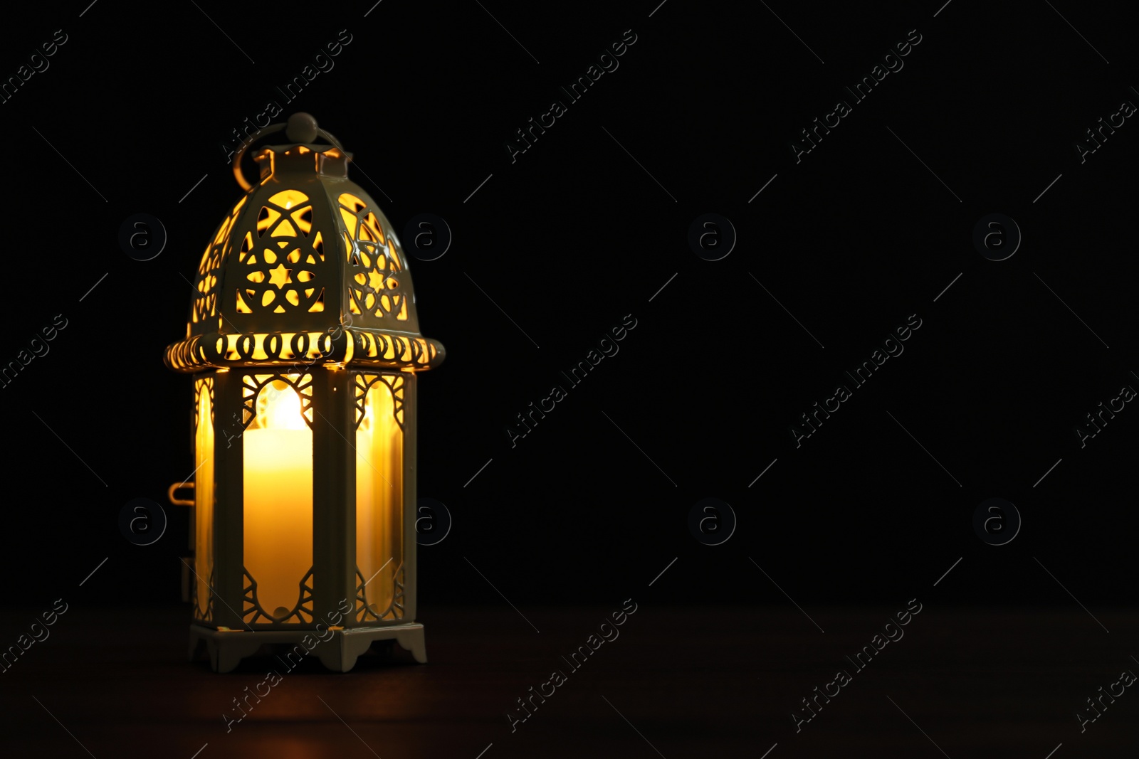 Photo of Decorative Arabic lantern on wooden table against black background, space for text