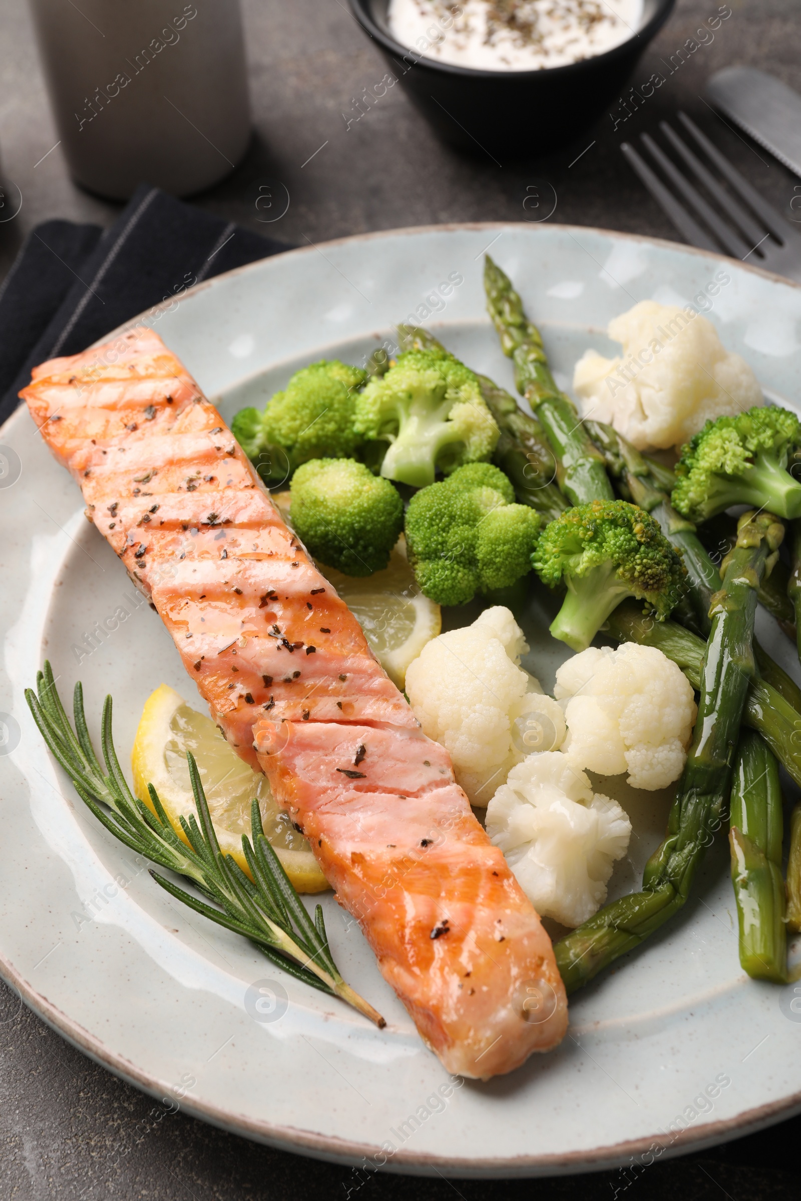 Photo of Healthy meal. Piece of grilled salmon, vegetables, lemon, asparagus and rosemary served on grey table, closeup