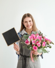 Photo of Female florist holding small chalkboard and bouquet on light background