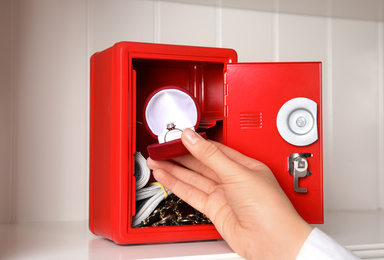Photo of Woman putting jewelry into red steel safe on shelf, closeup