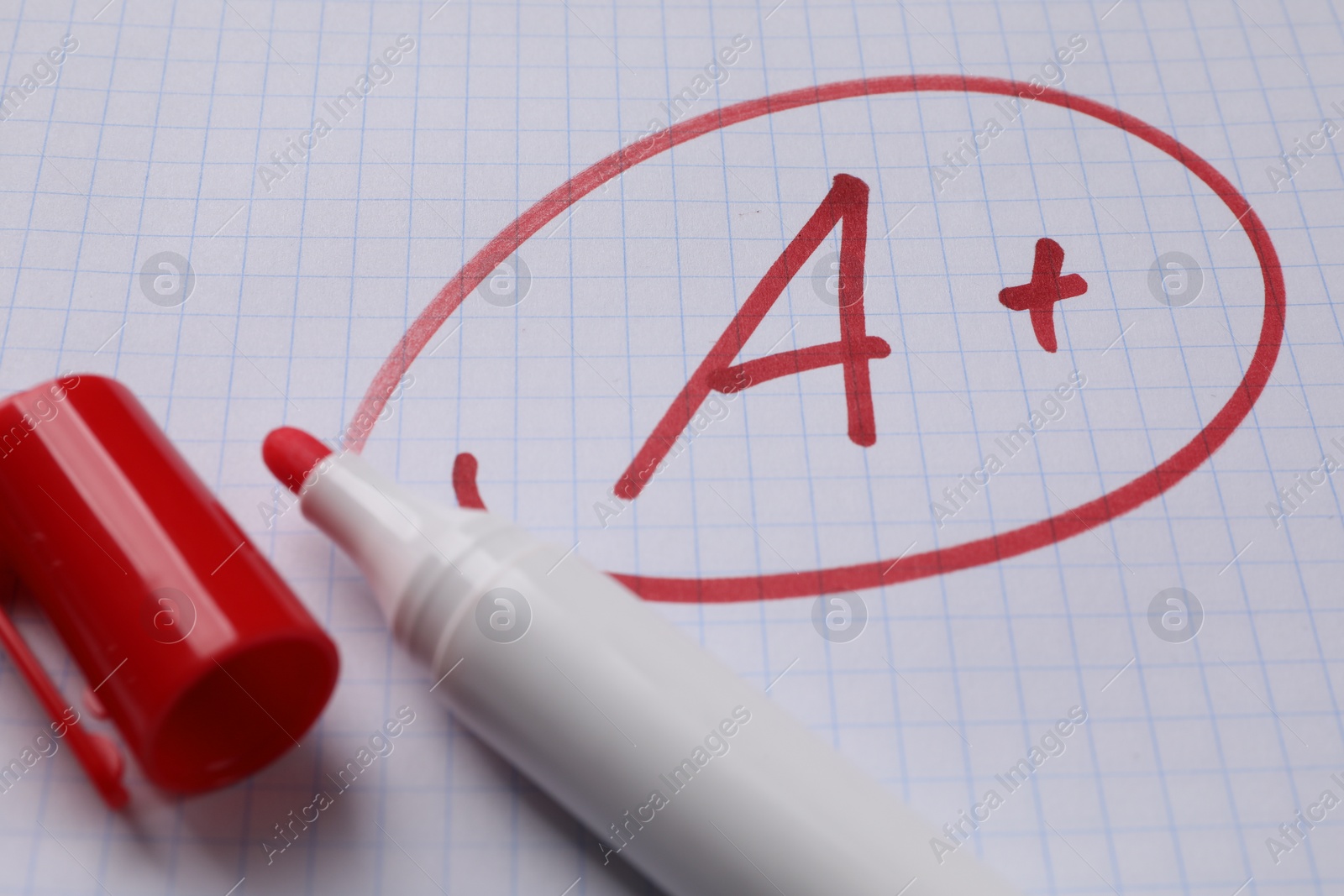 Photo of School grade. Red letter A with plus symbol on notebook paper and marker, closeup