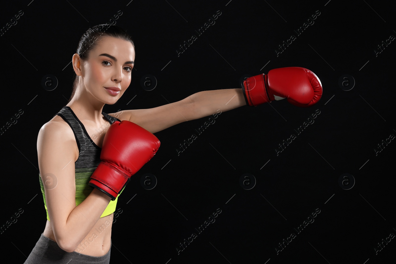 Photo of Beautiful woman in boxing gloves training on black background. Space for text