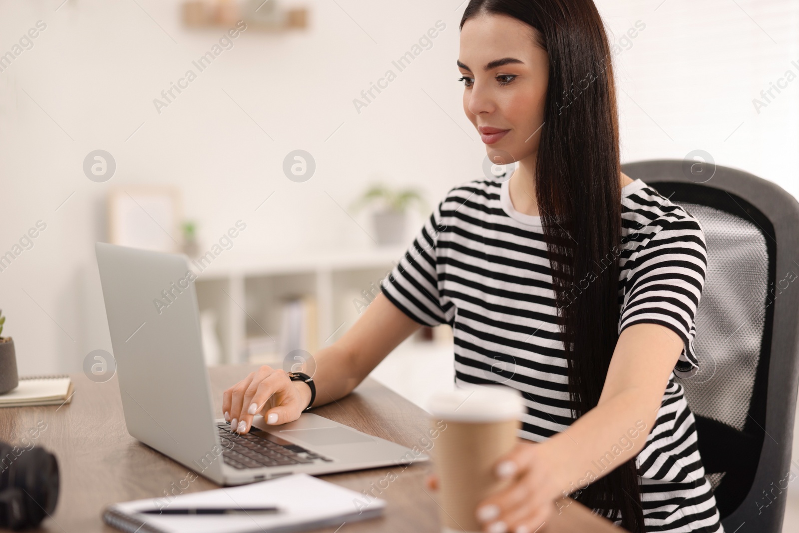 Photo of Young woman watching webinar at table in room