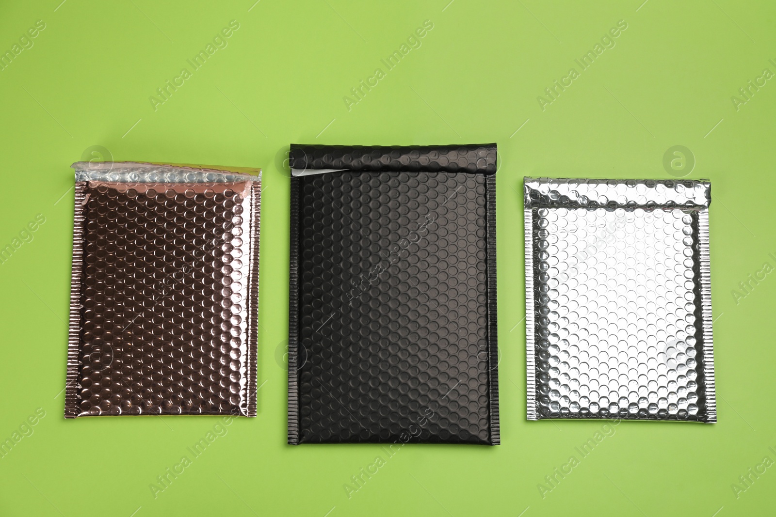 Photo of Three padded envelopes with bubble wrap on green background, flat lay