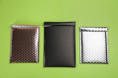 Photo of Three padded envelopes with bubble wrap on green background, flat lay