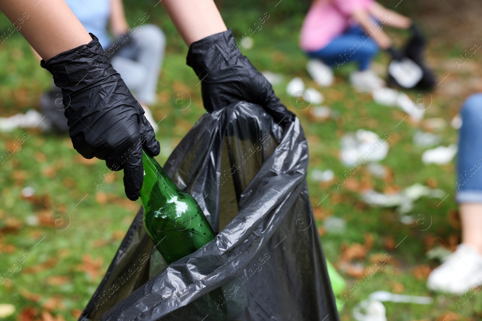 Photo of Woman with plastic bag collecting garbage in park, closeup