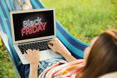 Image of Black Friday. Woman shopping online using laptop in hammock
