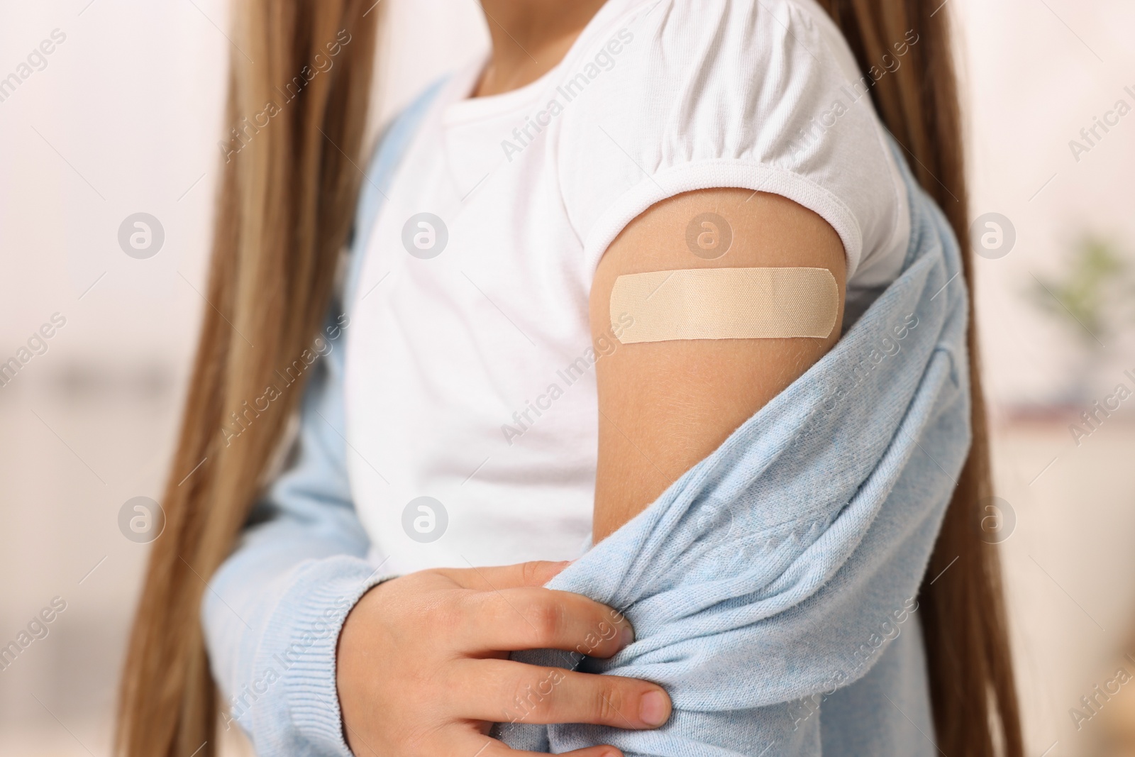 Photo of Girl with sticking plaster on arm after vaccination indoors, closeup