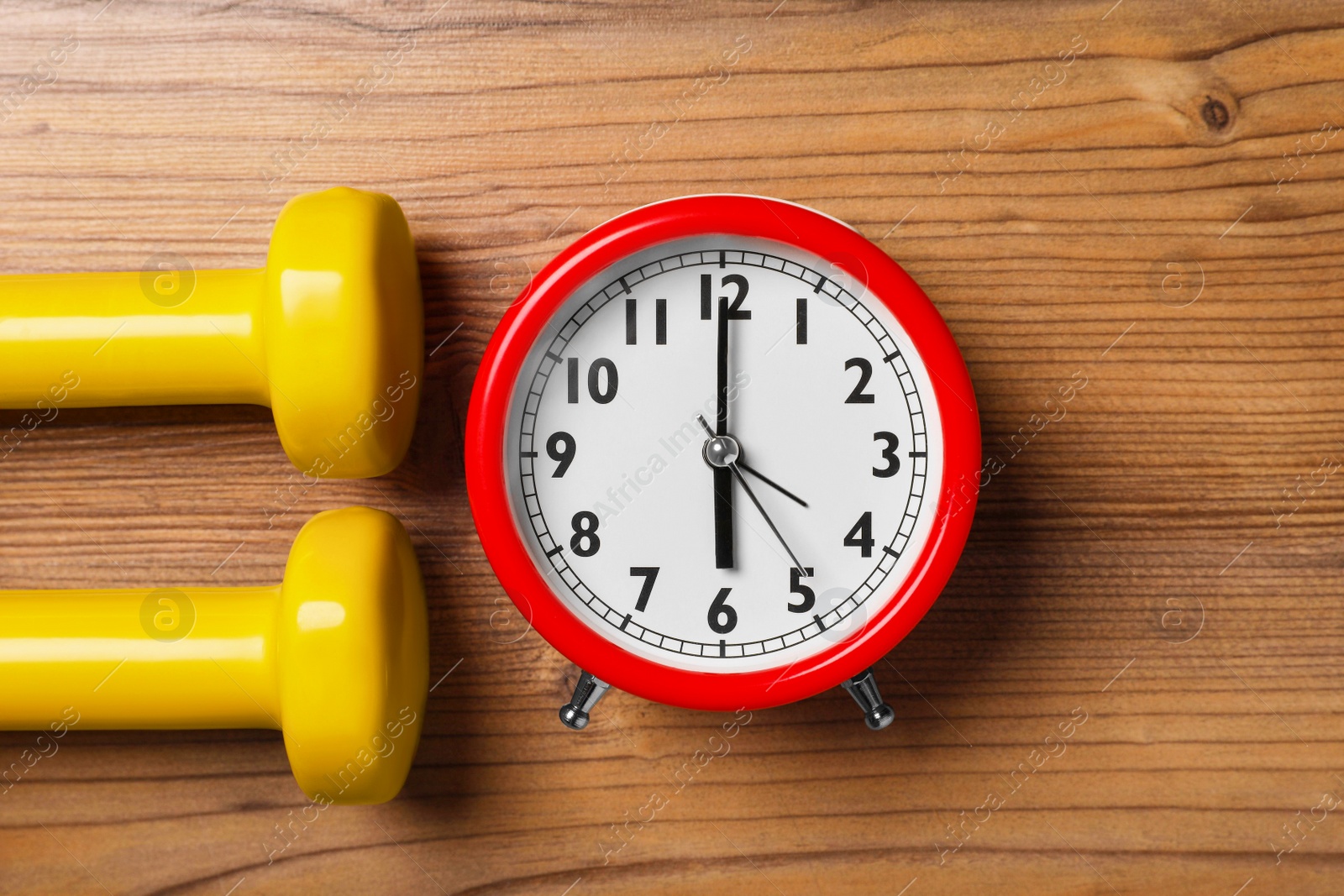 Photo of Alarm clock and dumbbells on wooden table, flat lay. Morning exercise