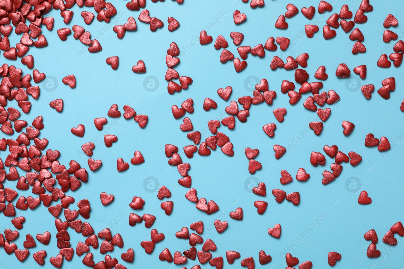 Photo of Bright heart shaped sprinkles on light blue background, flat lay