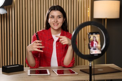 Smiling technology blogger pointing at smartphone while recording video at home
