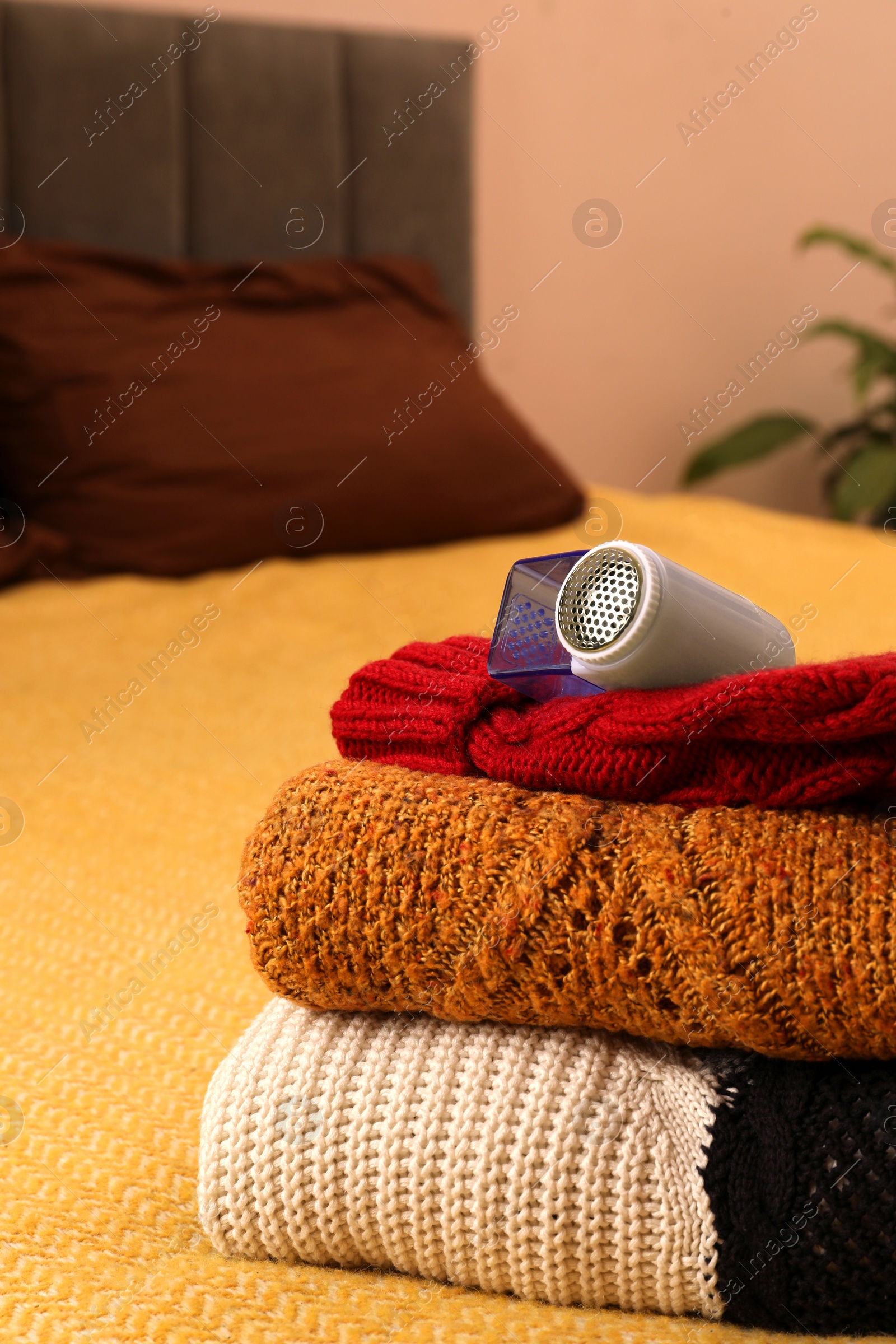 Photo of Modern fabric shaver and knitted clothes on bed indoors, closeup. Space for text