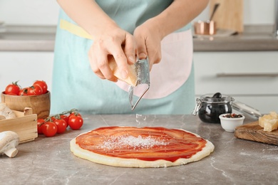 Photo of Woman grating cheese onto pizza on table