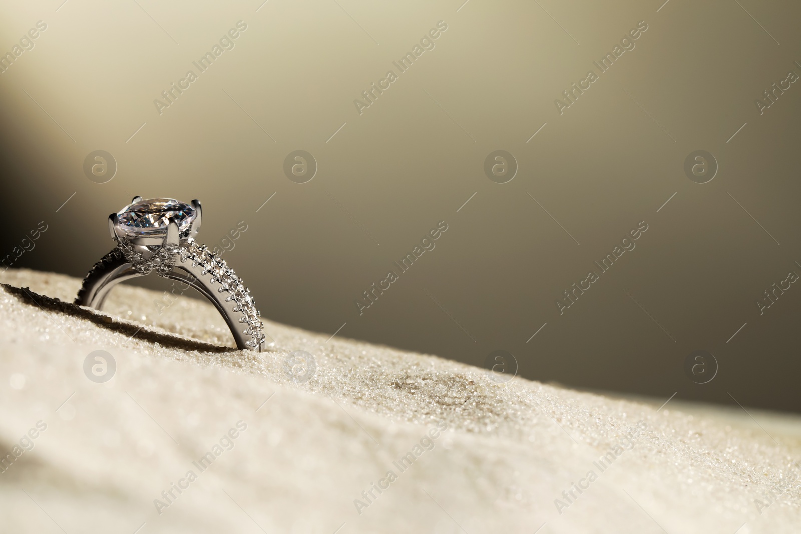 Photo of Luxury jewelry. Stylish presentation of ring in sand against grey background, closeup. Space for text