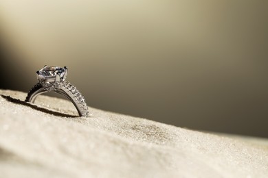 Photo of Luxury jewelry. Stylish presentation of ring in sand against grey background, closeup. Space for text