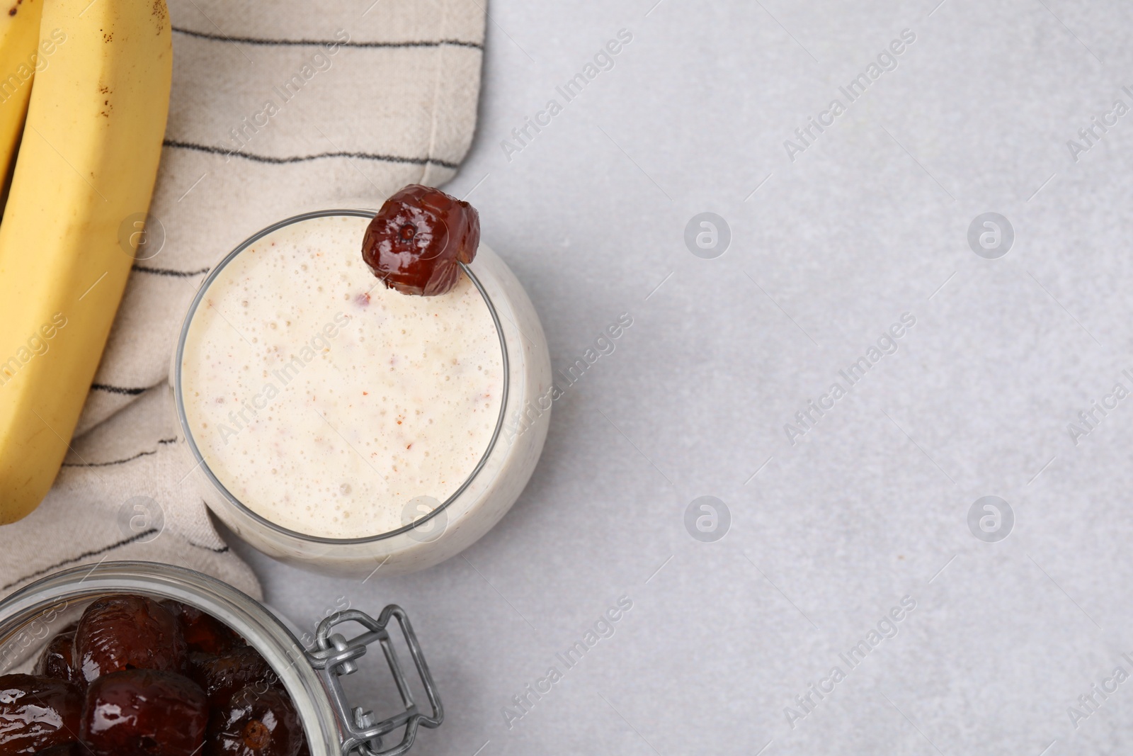 Photo of Glass of delicious date smoothie with mint, dried fruits and bananas on light grey table, flat lay. Space for text