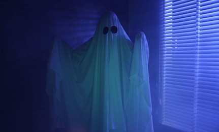 Creepy ghost. Woman covered with sheet near window in blue light