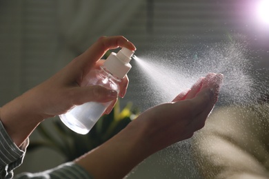 Photo of Woman spraying antiseptic onto hand indoors, closeup