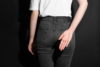 Photo of Woman showing open palm behind her back on black background, back view