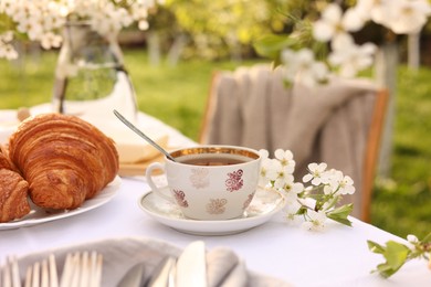 Stylish table setting with beautiful spring flowers, tea and croissants in garden