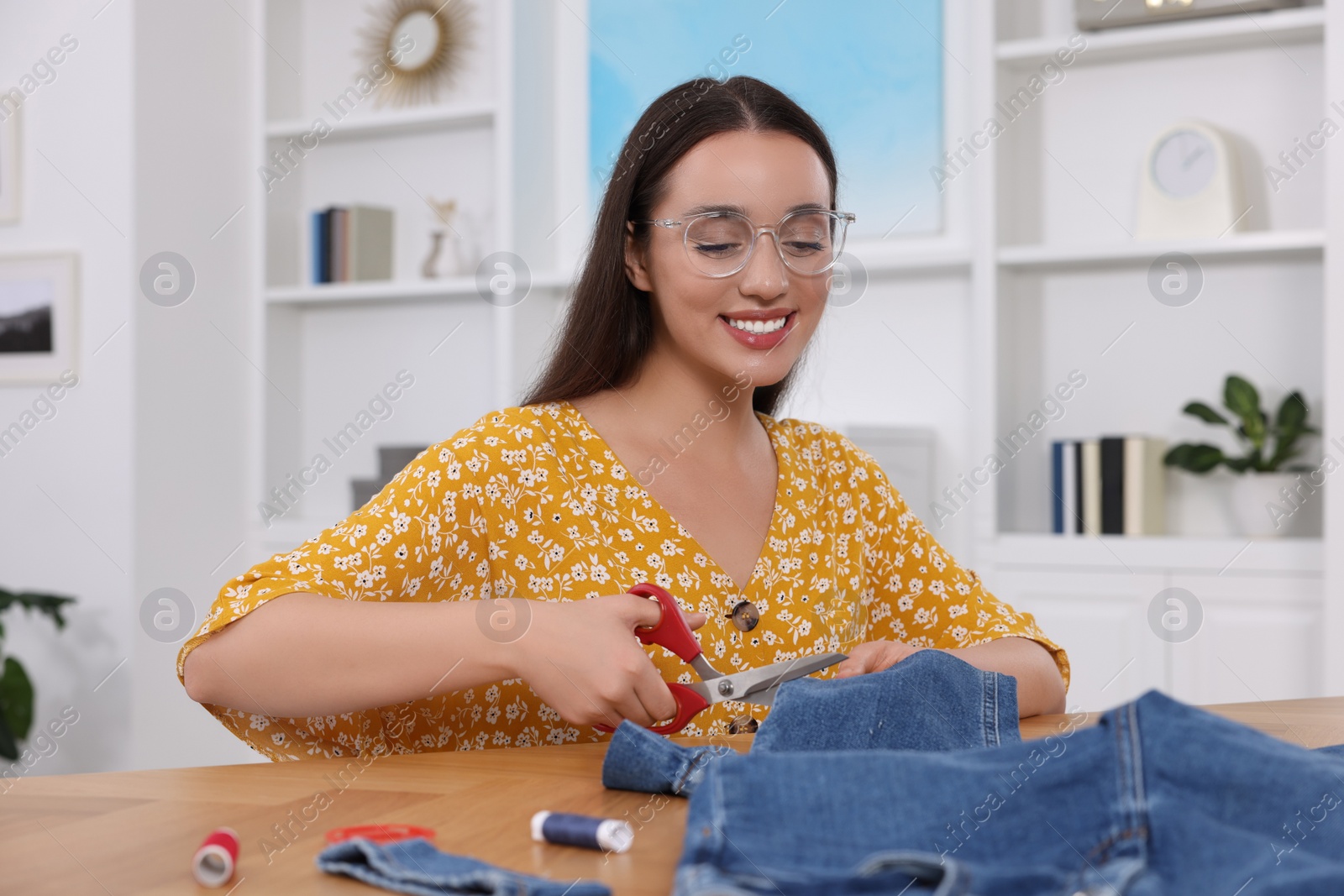 Photo of Happy woman cutting hem of jeans at table indoors