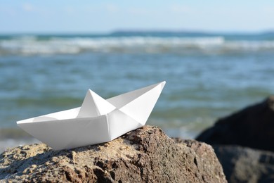 Photo of White paper boat on rock near sea, space for text