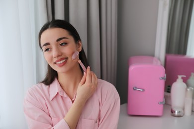 Photo of Woman doing face massage at dressing table with cosmetic refrigerator indoors