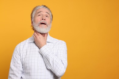 Senior man suffering from sore throat on yellow background, space for text. Cold symptoms