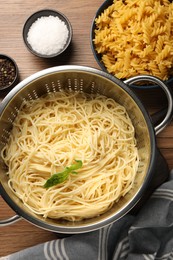 Cooked pasta in metal colander and spices on wooden table, flat lay