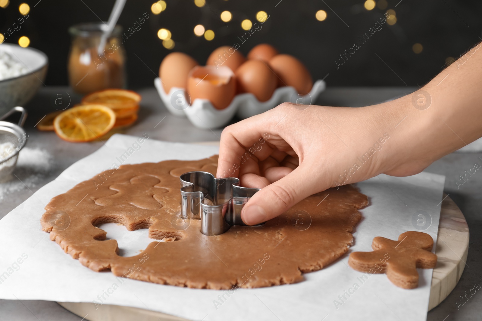 Photo of Woman making Christmas gingerbread man cookies at light grey table, closeup