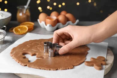 Woman making Christmas gingerbread man cookies at light grey table, closeup