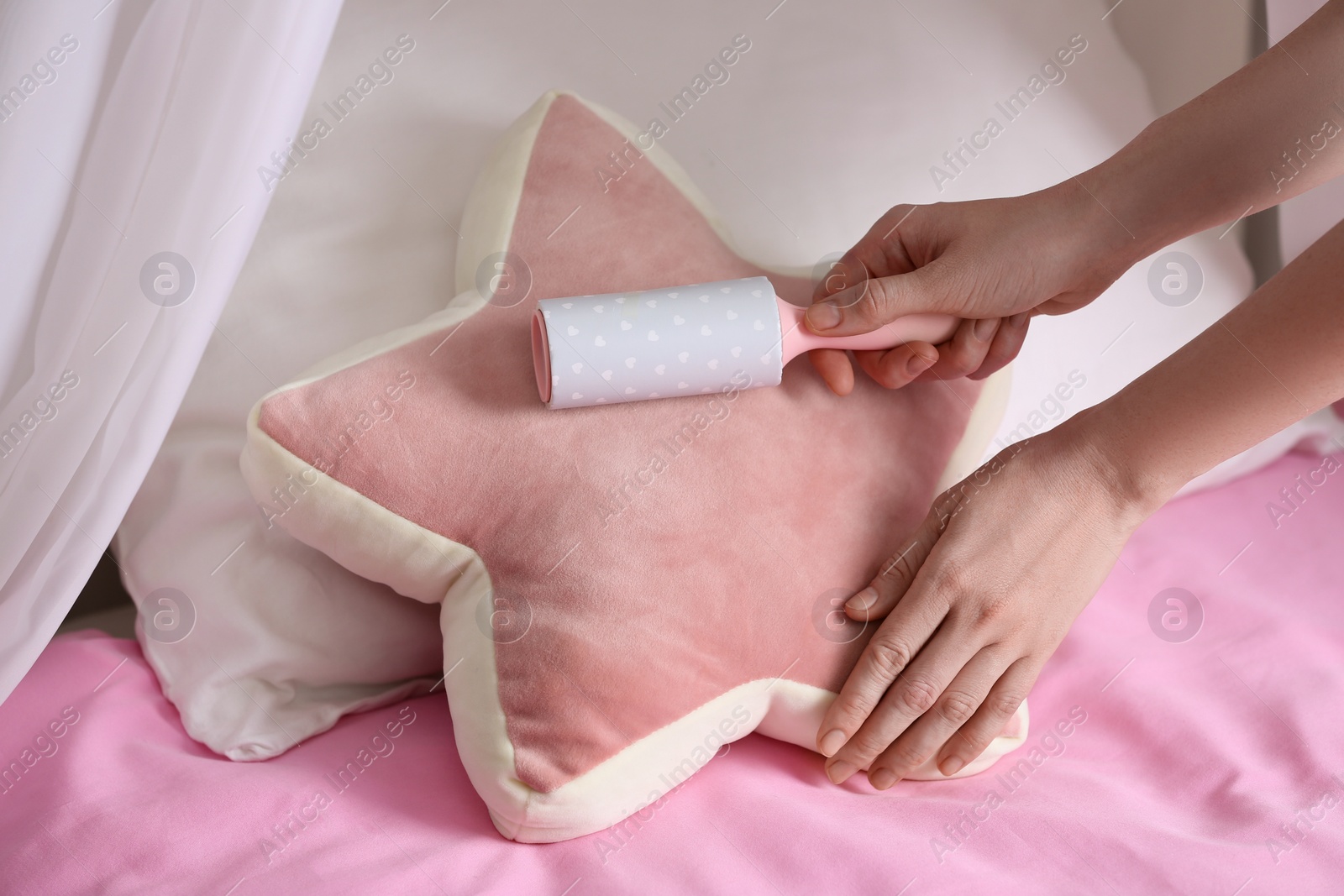 Photo of Woman cleaning star shaped cushion with lint roller at home, closeup