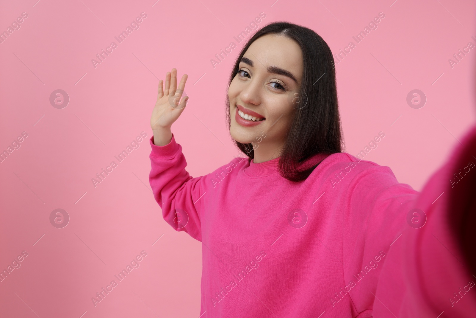 Photo of Smiling young woman taking selfie on pink background, space for text