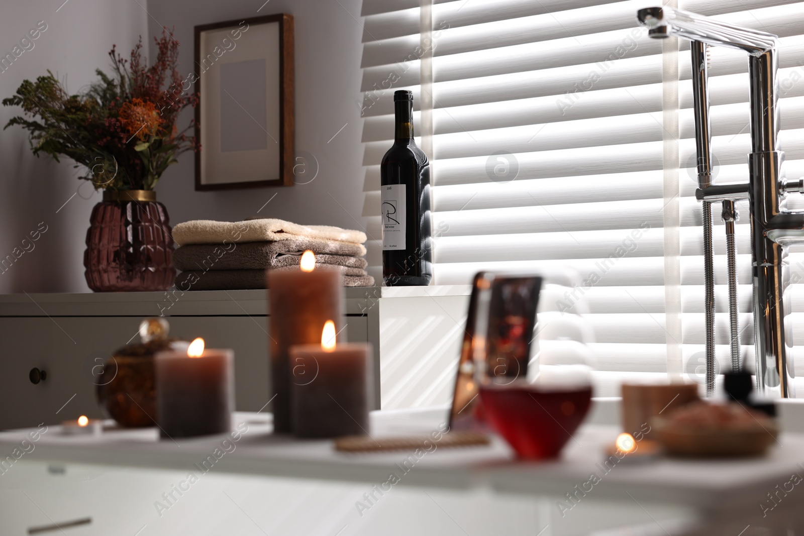 Photo of Bottle of wine, towels and flowers on chest of drawers in bathroom, selective focus