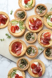 Different delicious canapes on white marble table, flat lay